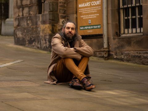 Marcas Mac an Tuairneir seated outdoors, cross legged